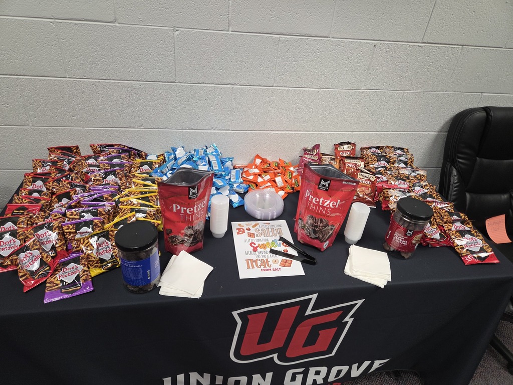 A table covered in a black tablecloth, displaying snacks, cups, and a sign that reads "Union Grove".