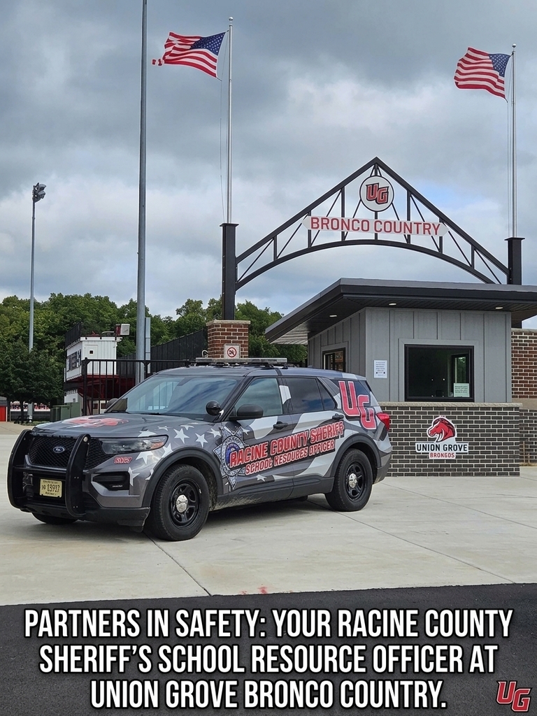 Police car parked in front of a building with "BRONCO COUNTRY" above it. Two flags on poles behind it.