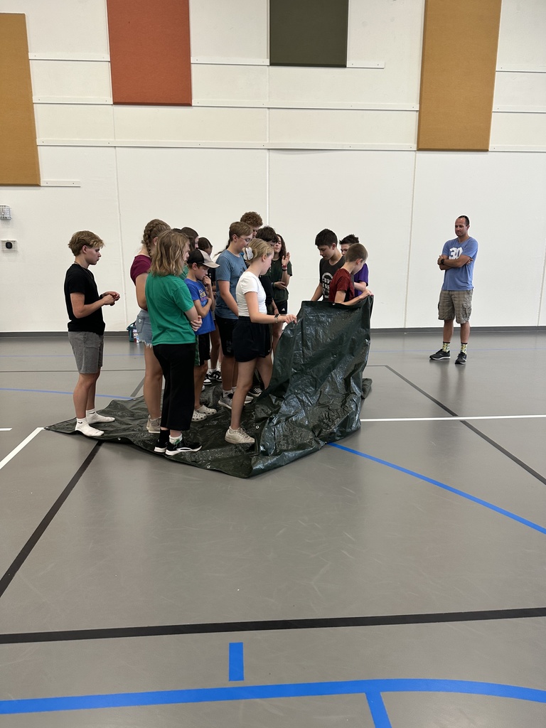 students standing on a tarp working on a team-building exercise