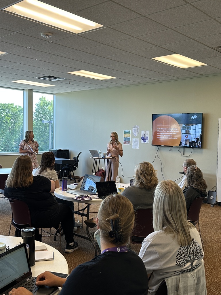 two presenters at the front of a classroom speaking to a group of teachers