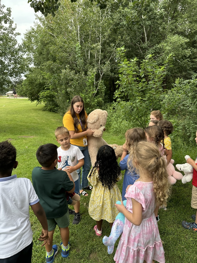 teacher holding an oversized teddy bear and talking to a group of students