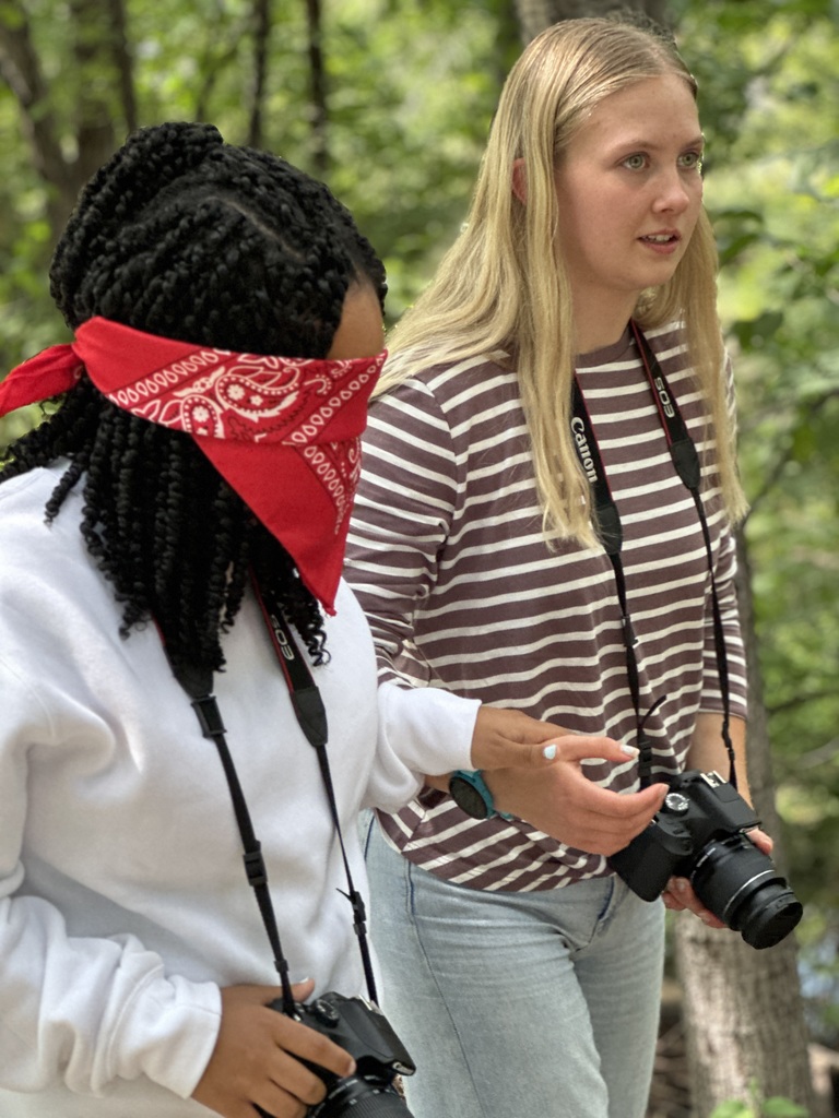 students guiding a blindfolded classmate around so they can take photographs outside