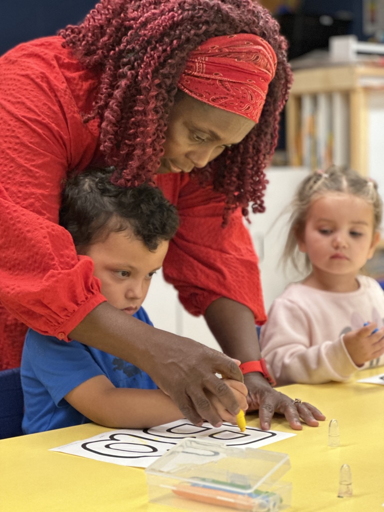 pre-k teacher helping a student write