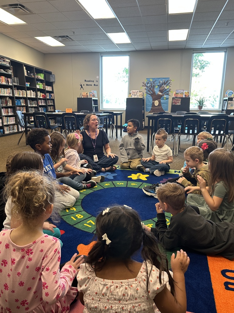 librarian sitting on the floor in a circle with  kindergarten students