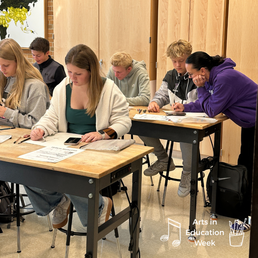 art teacher working with a group of students at their desk
