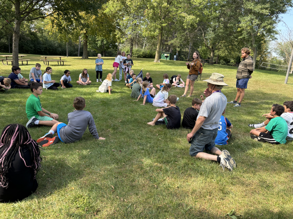 6th grade students sitting on the grass listening to a guest speaker