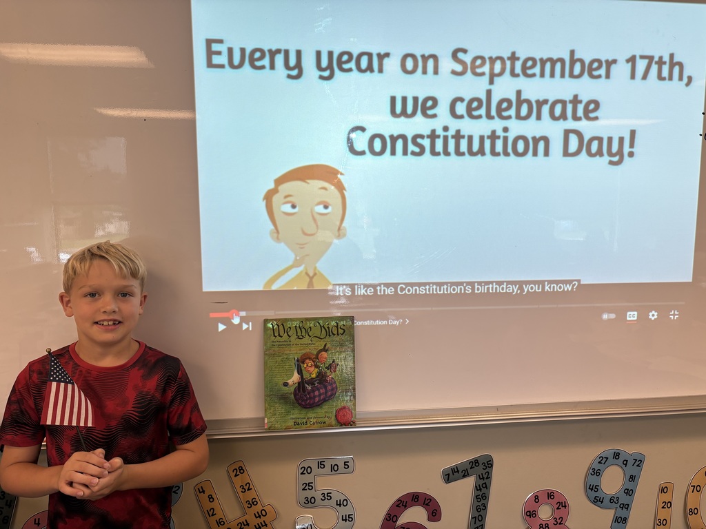 third grade student holding a flag and a book