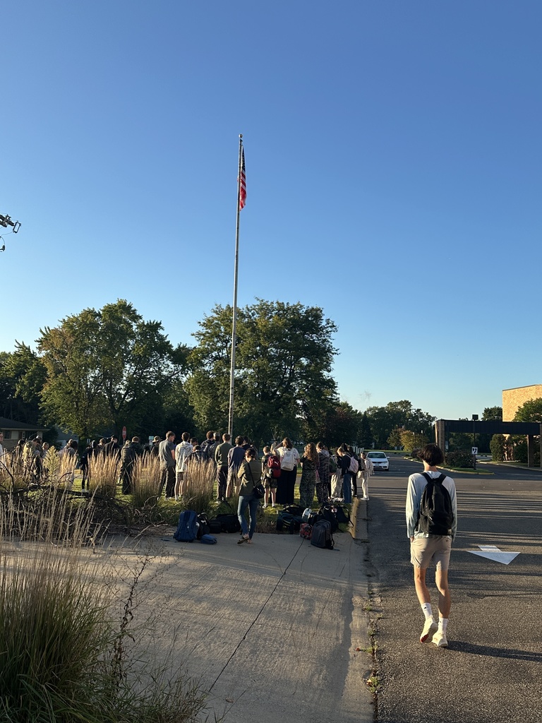 students and parents gathered around a flagpole for a time of prayer