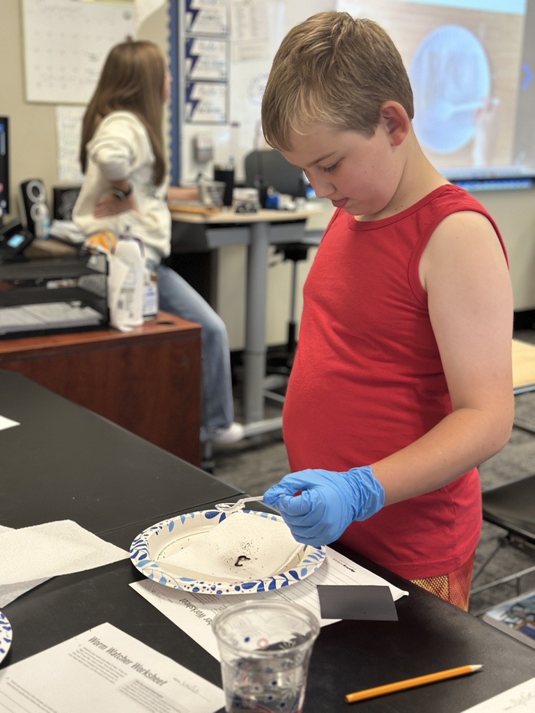5th grade students looking at a worm on a paper plate