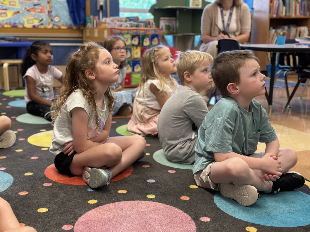 kindergarten students sitting on their classroom rug listening to someone read a book