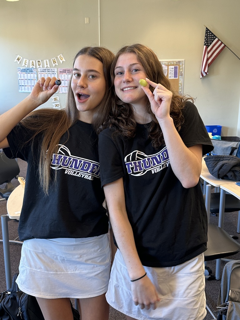 two female students holding a piece of fruit and smiling