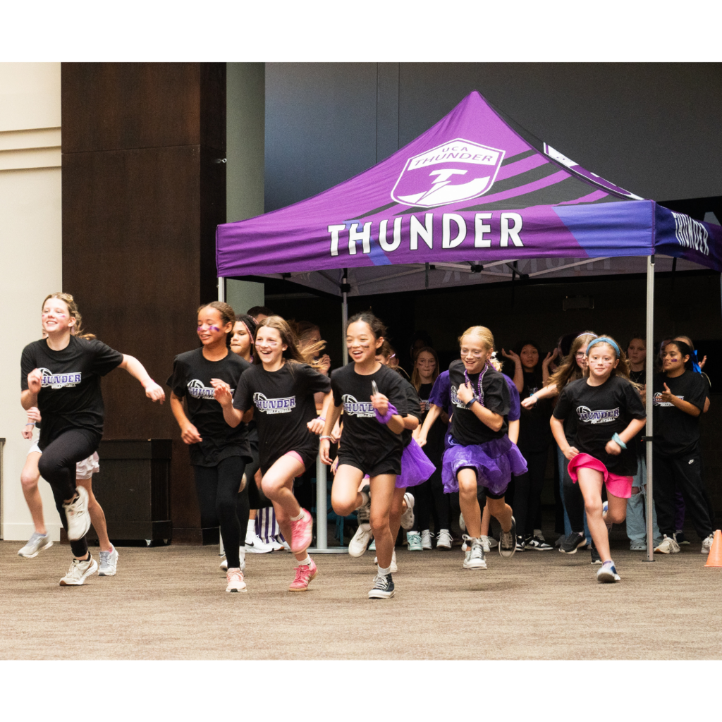 middle school volleyball players running to the center of the room as they're being introduced at a pep fest