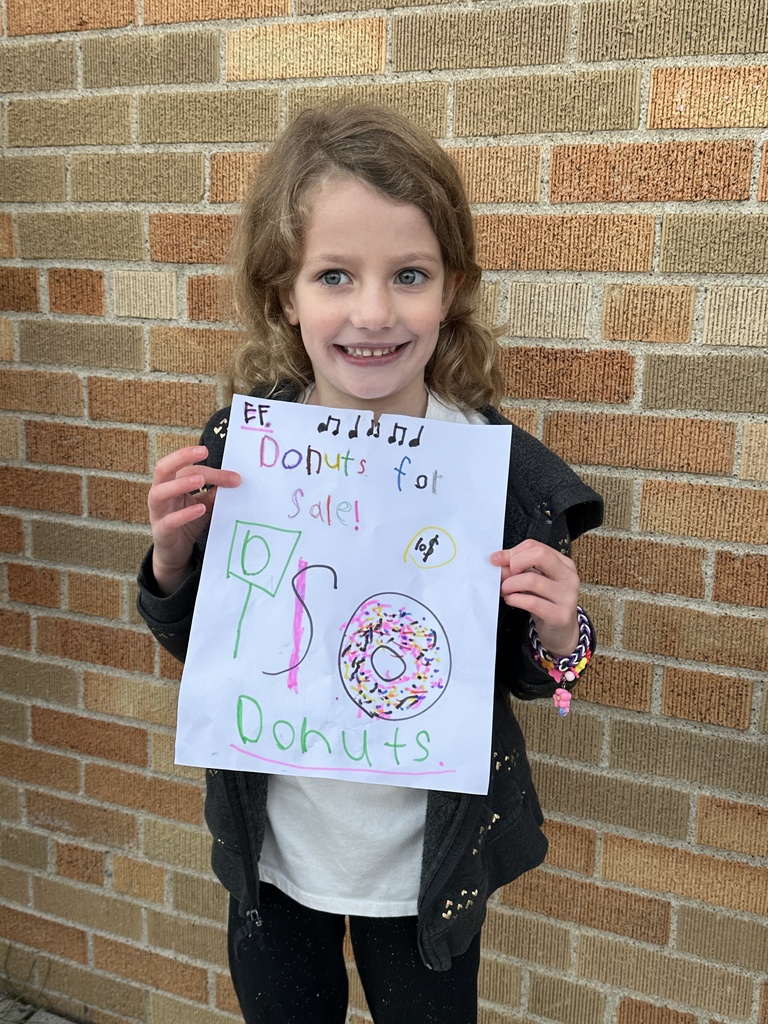 1st grade girl holding a sign she made for selling donuts