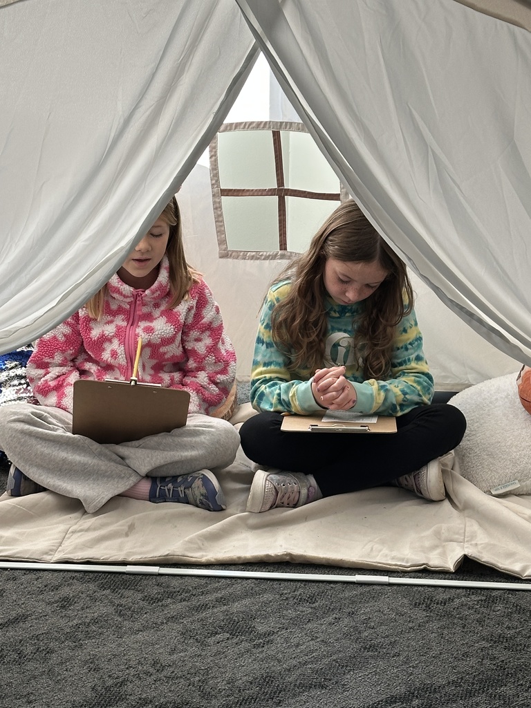 two girls sitting inside a reading tent, praying for each other