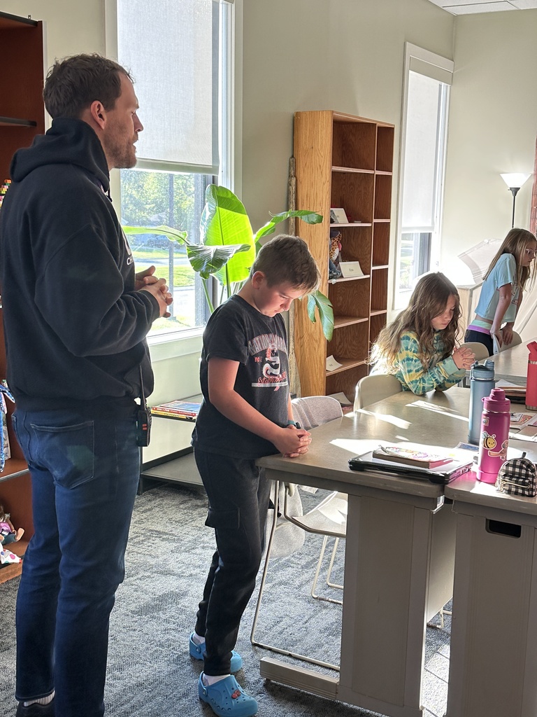 teacher praying at the front of his classroom with students standing by their desks and praying