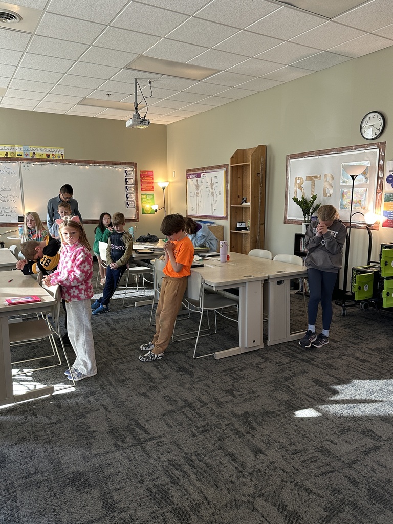 teacher praying at the front of his classroom with students standing by their desks and praying
