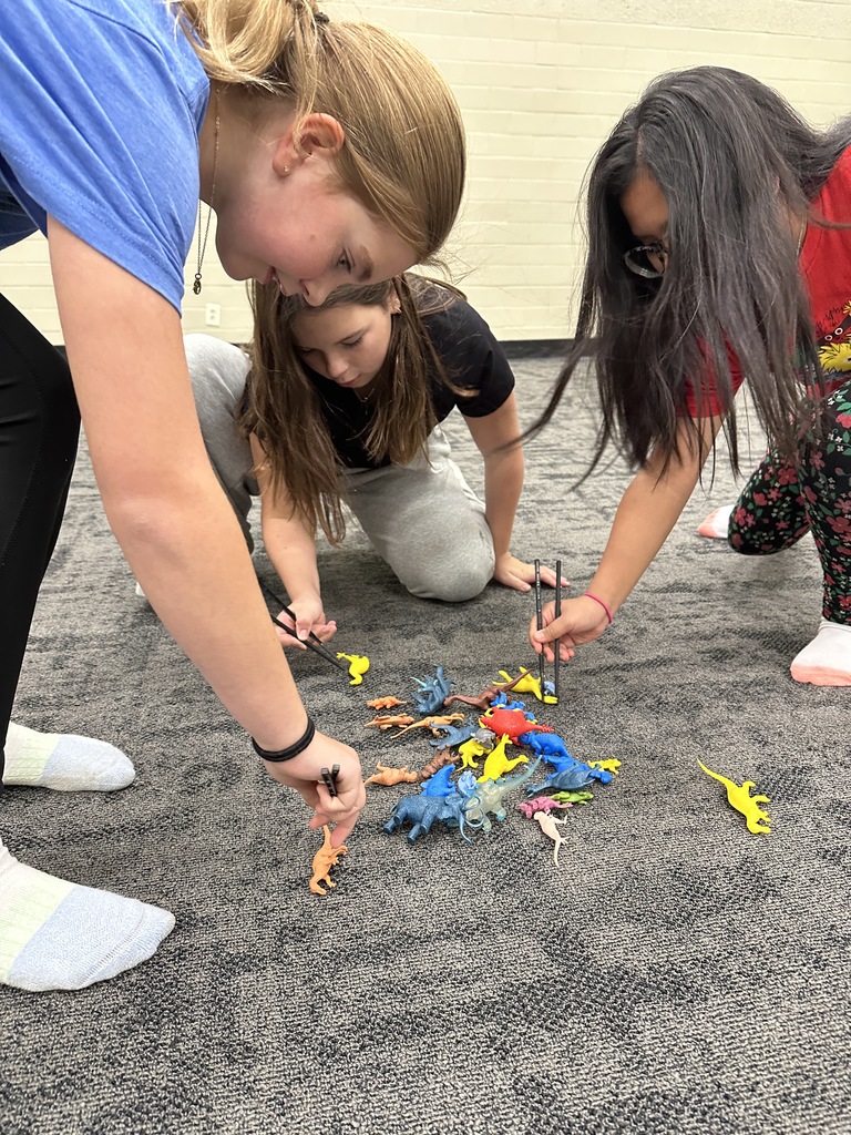 6th grade students participating in a relay race, trying to pick up a toy dinosaur with chopsticks