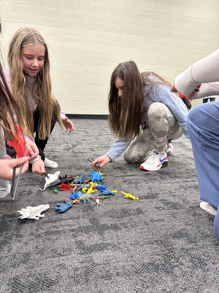 6th grade students participating in a relay race, trying to pick up a toy dinosaur with chopsticks