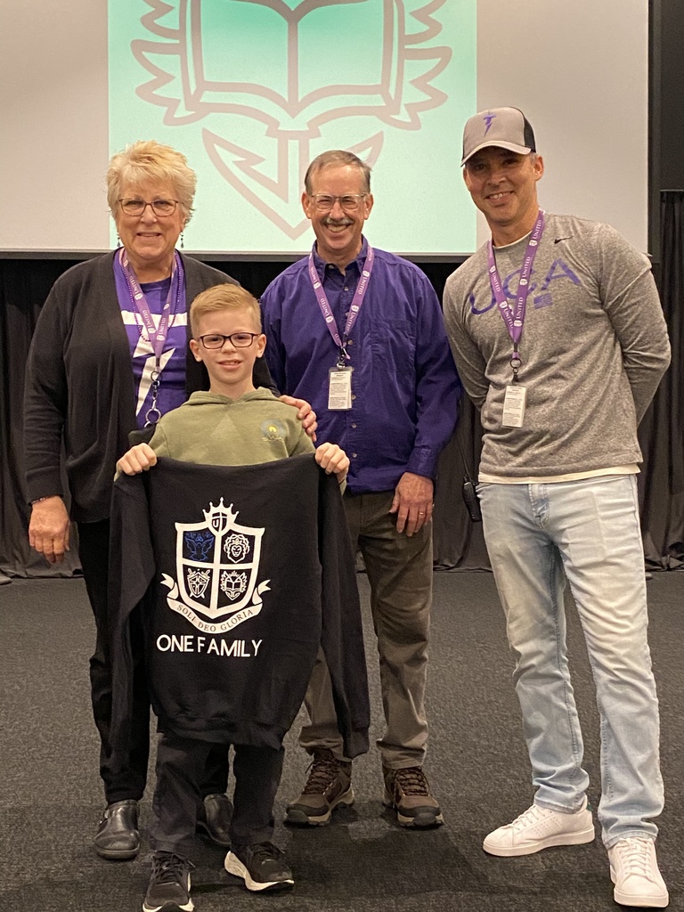 elementary student holding a sweatshirt he won standing with his teacher, the principal and the head of school