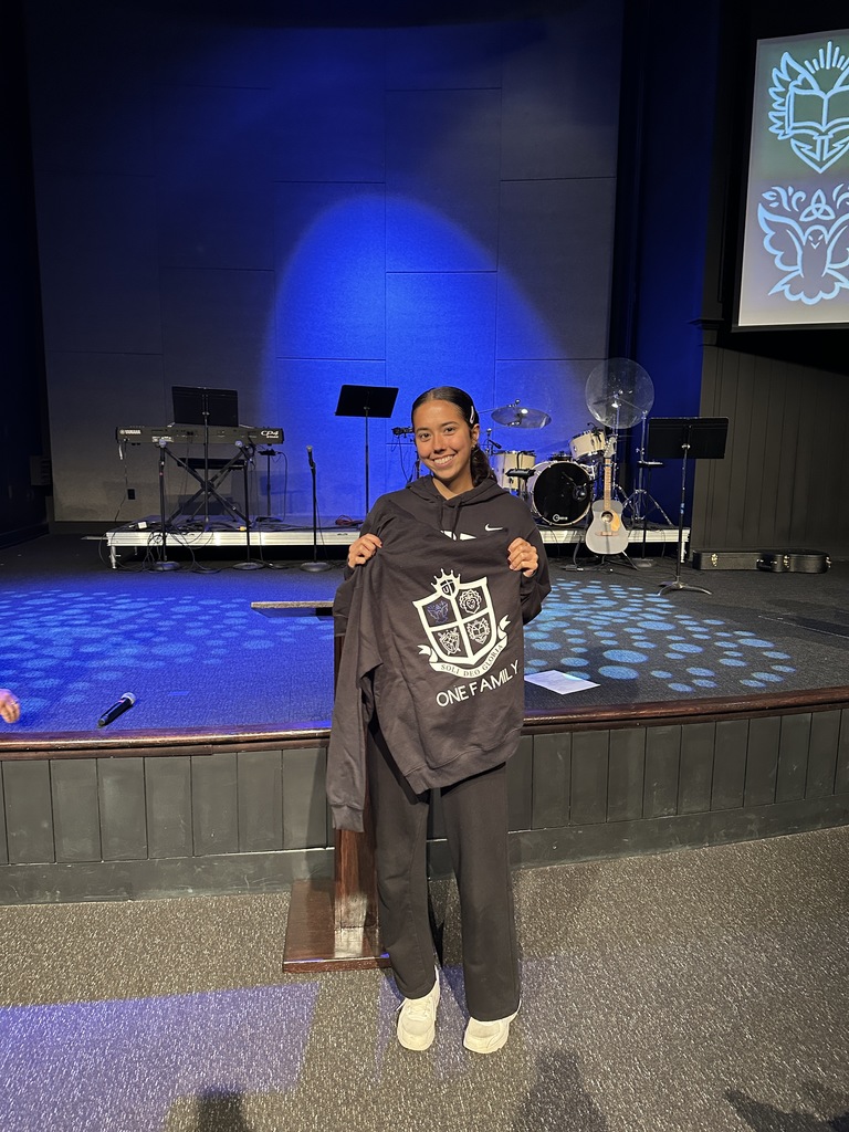 high school student holding up a sweatshirt that she was given after earning "Student of the Quarter"
