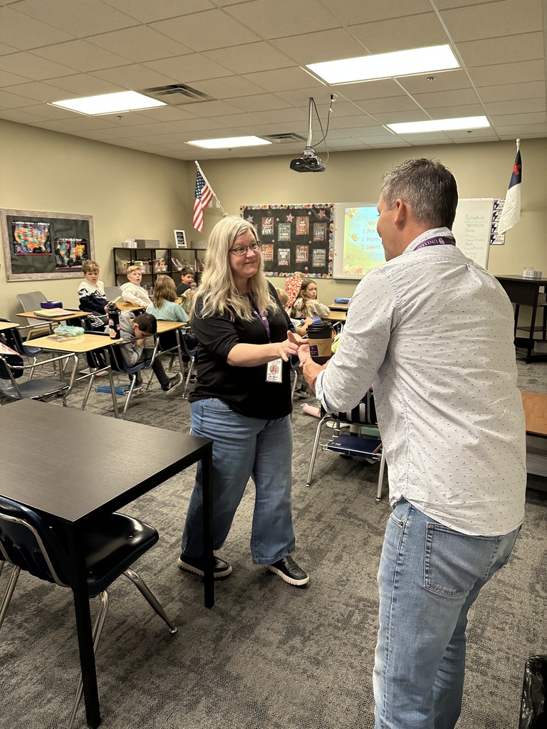 head of school delivering a coffee drink to a 4th grade teacher with her students watching in the background