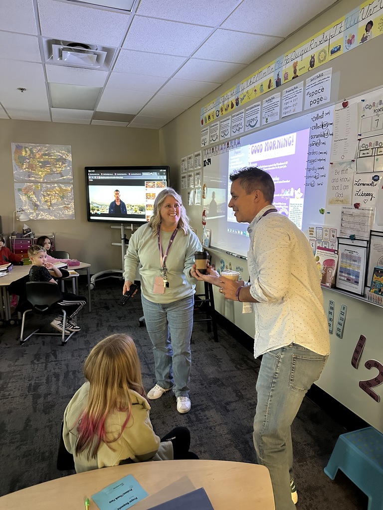 head of school delivering a coffee drink to a 4th grade teacher with her students watching in the background