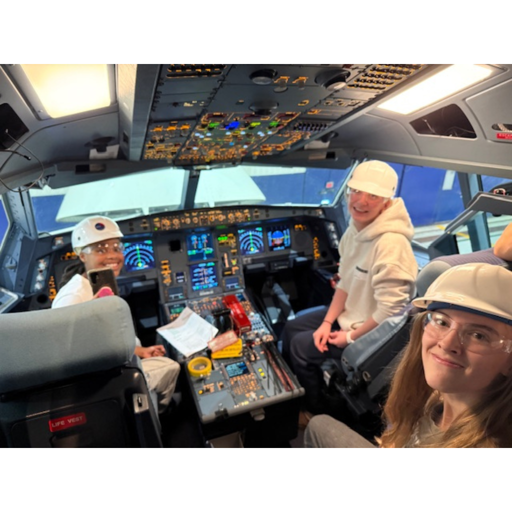three female students sitting in the cockpit of a Delta plane
