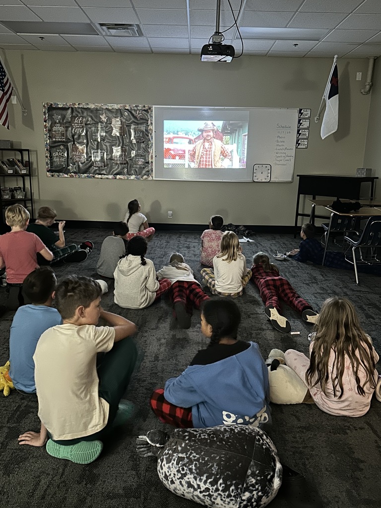 4th grade students laying on the floor in pajamas watching a movie on the projector