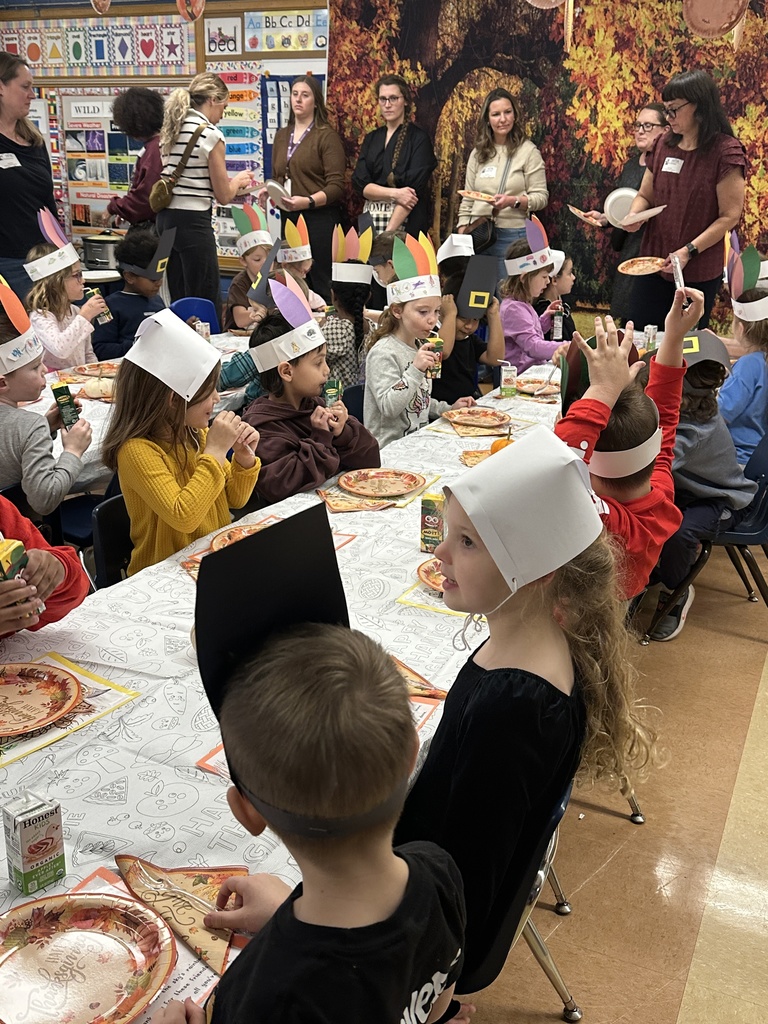 kindergarten students sitting at tables eating a thanksgiving feast with parent volunteers serving food