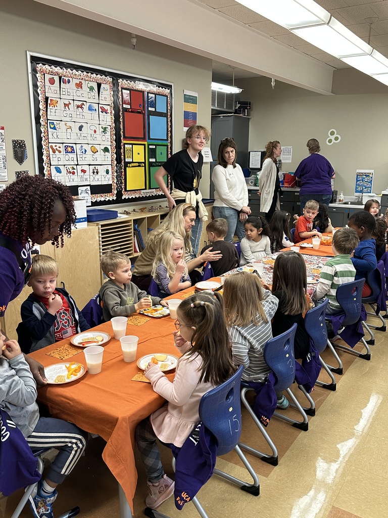 table of pre-k students eating snacks with parent volunteers standing in the background