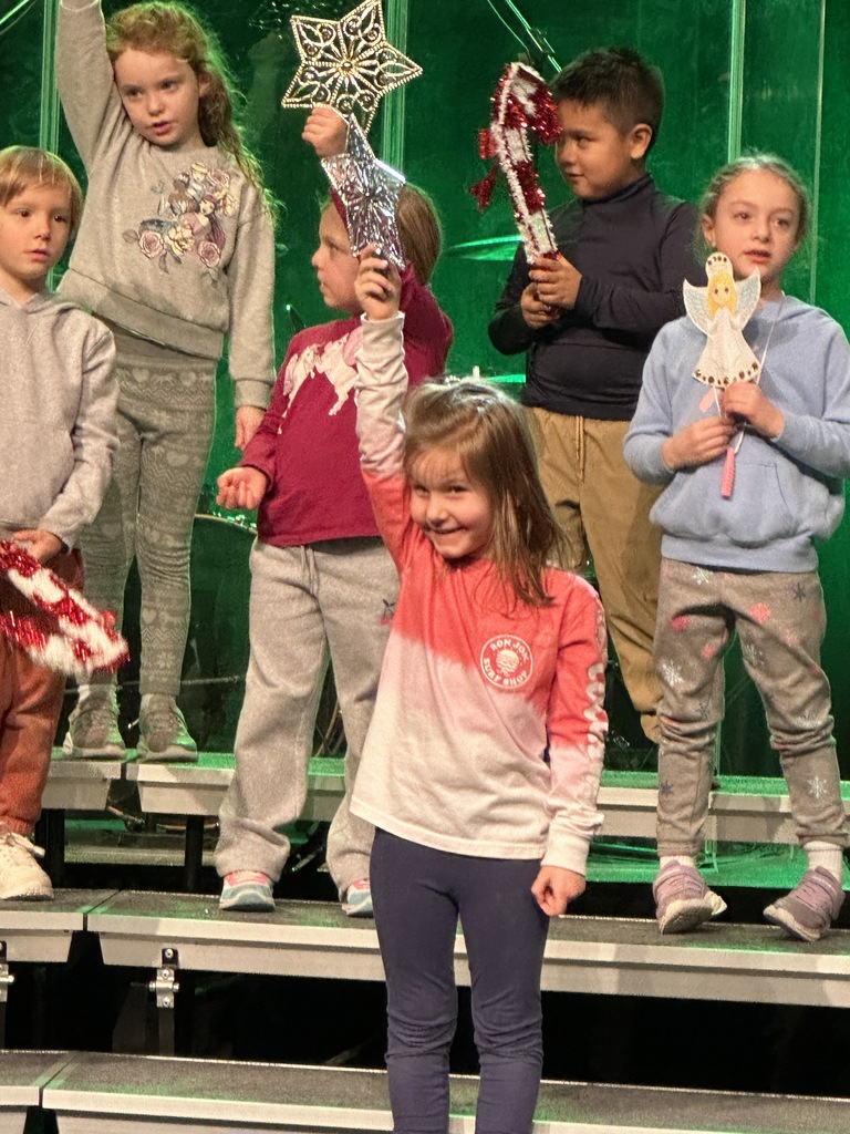 students singing on stage, some holding props