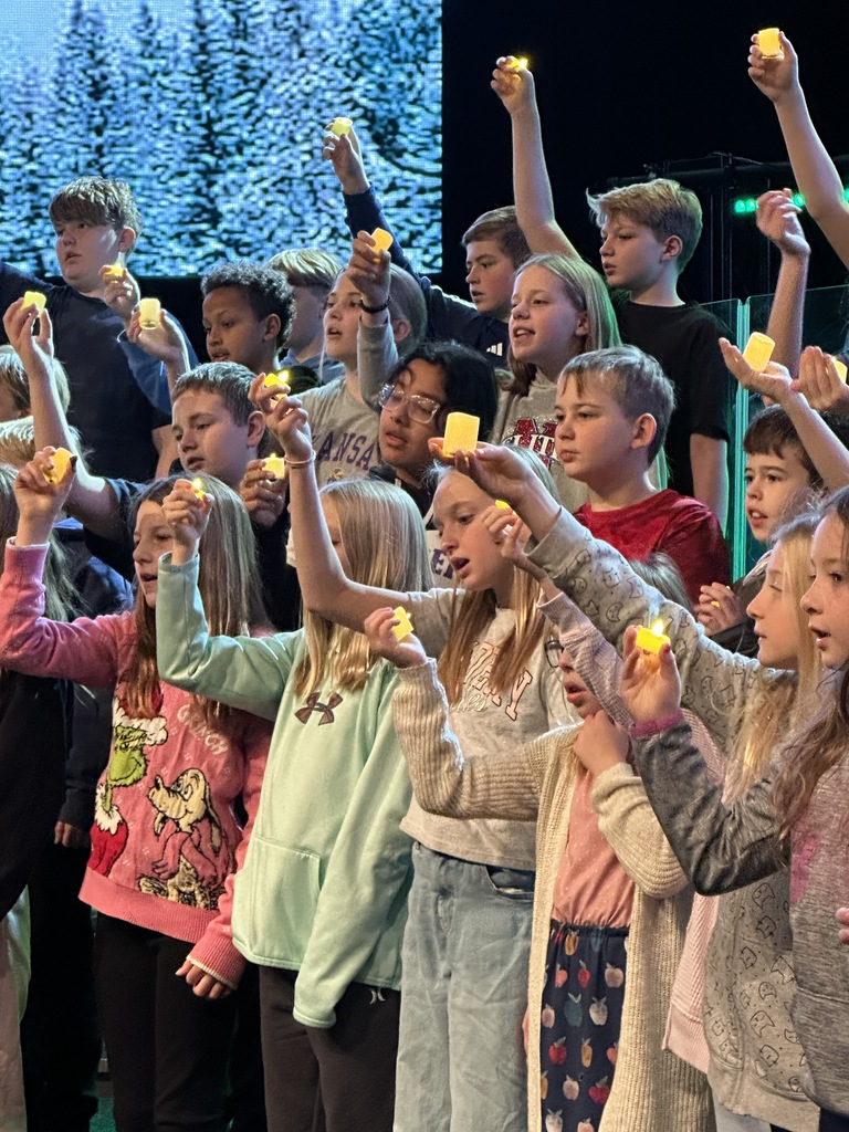students holding candles while singing on stage