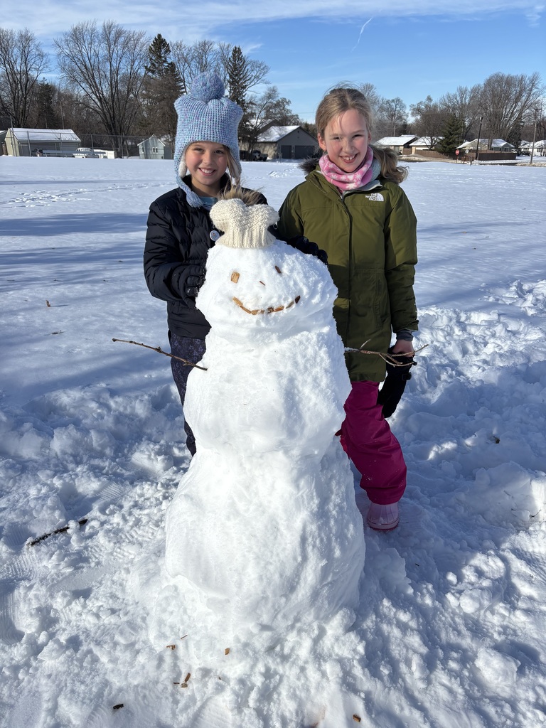 two elementary aged girls standing by a snowman they built