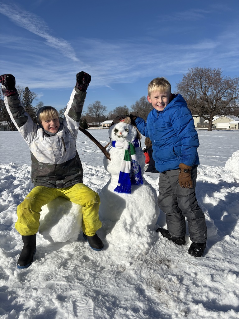 two elementary boys standing next to a snowman