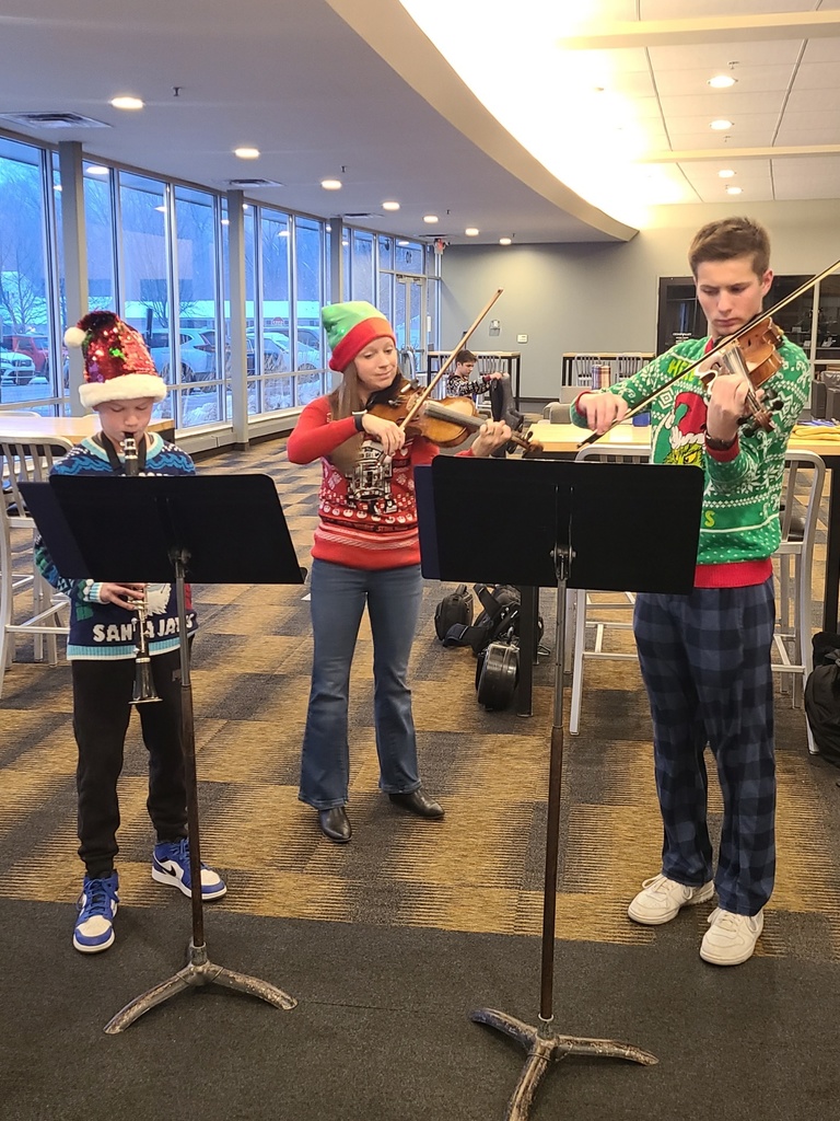 staff members singing christmas carols and playing instruments as students walk into the building