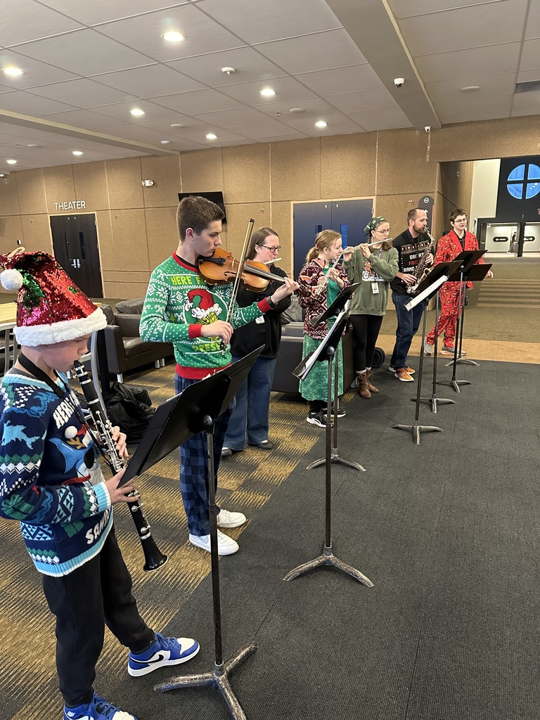 staff members singing christmas carols and playing instruments as students walk into the building