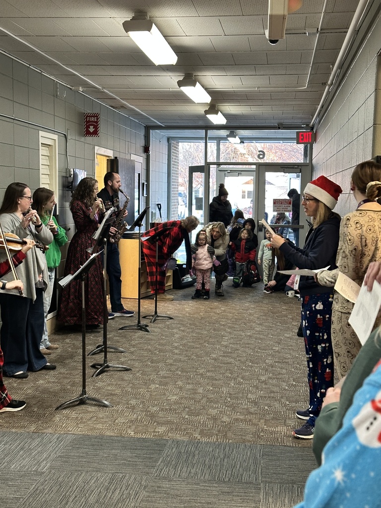 staff members singing christmas carols and playing instruments as students walk into the building