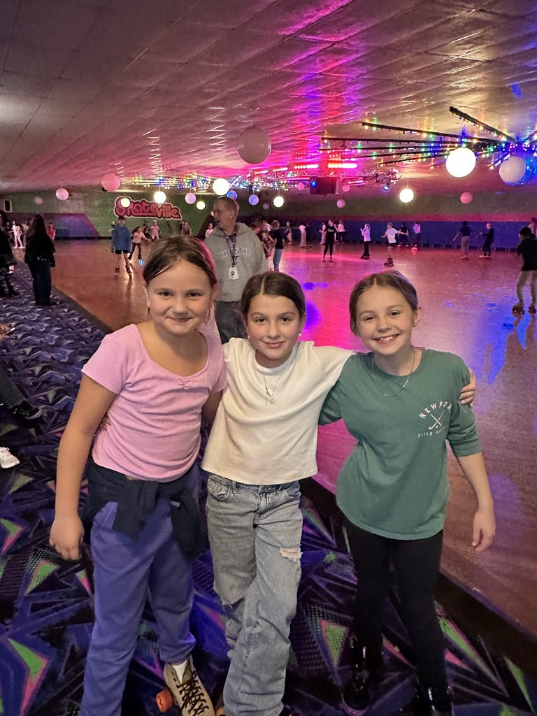 three elementary girls standing by a roller skating rink