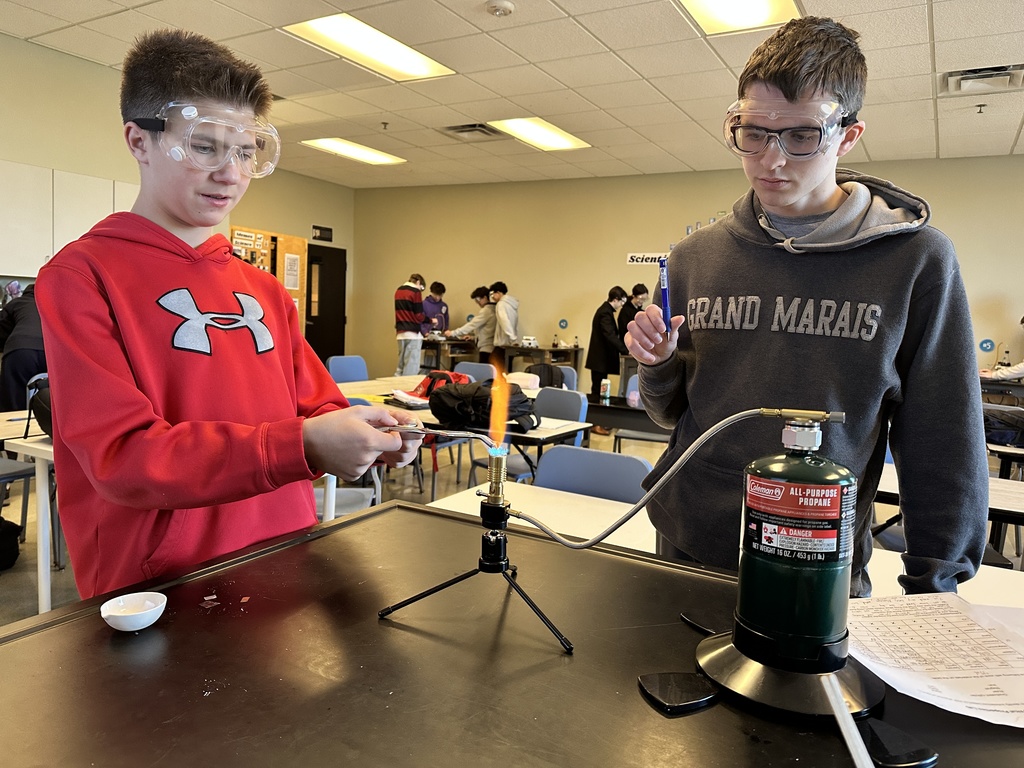 two male students performing flame tests in science class