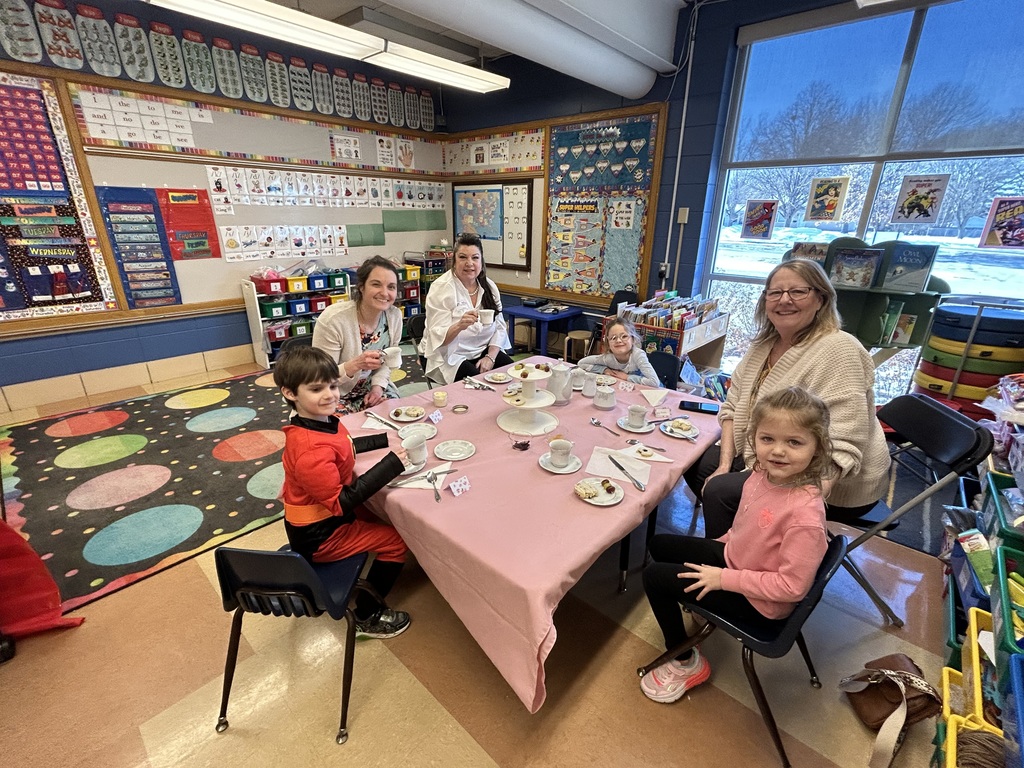 group of kindergarten students sitting at a table with special guests enjoying a tea party