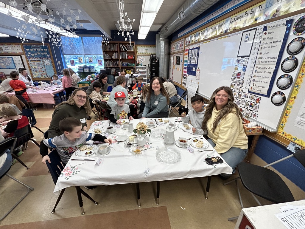group of kindergarten students sitting at a table with special guests enjoying a tea party