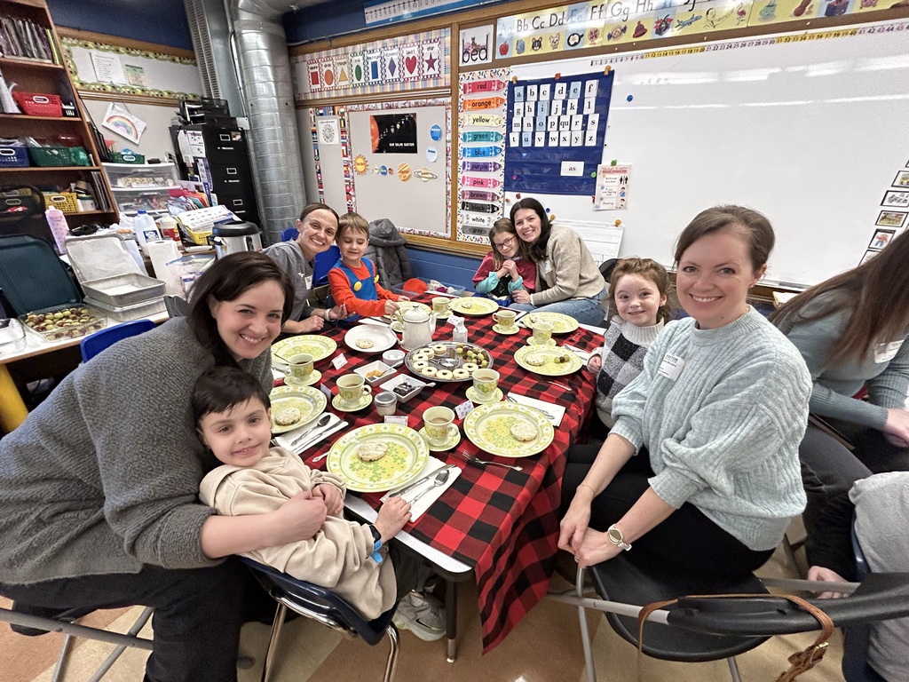 group of kindergarten students sitting at a table with special guests enjoying a tea party