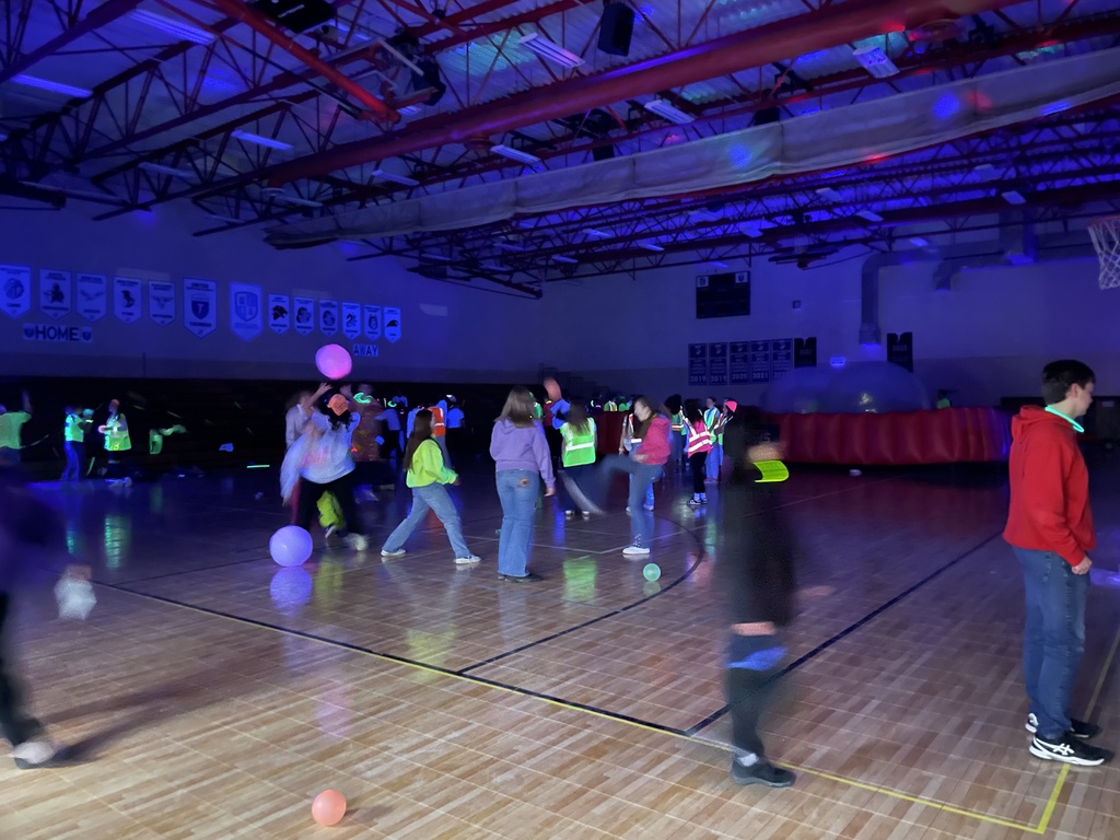 high school students dressed in neon playing in the gymnasium under black lights