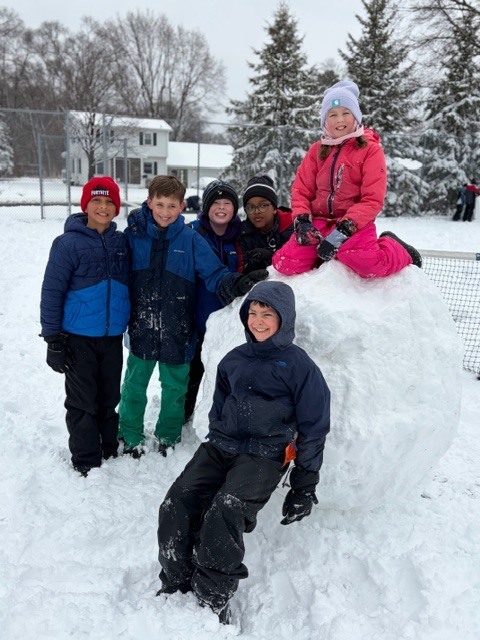 group of elementary students standing by a huge snowball