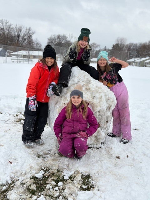 group of elementary students standing by a huge snowball