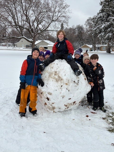 group of elementary students standing by a huge snowball
