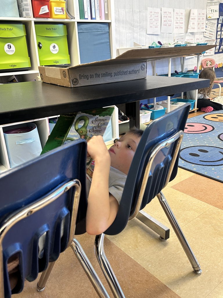 student laying on a chair under a table reading to himself