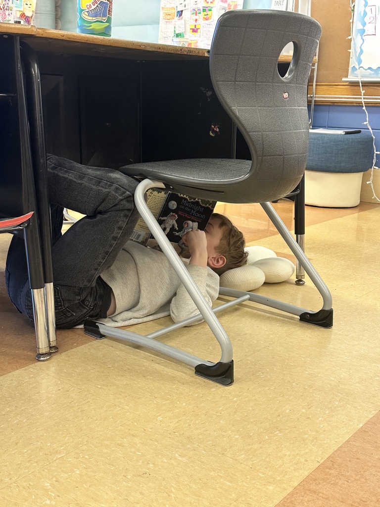 1st grade boy sitting on the floor under his desk quietly reading to himself