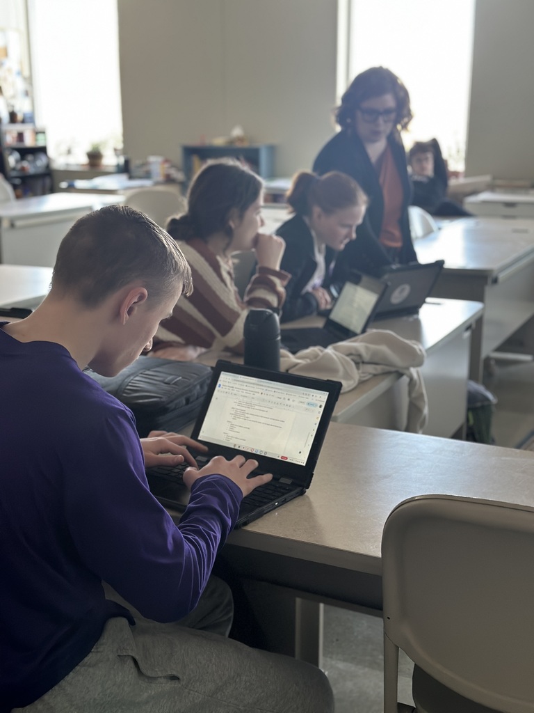 students working on their chromebooks and a teacher helping them