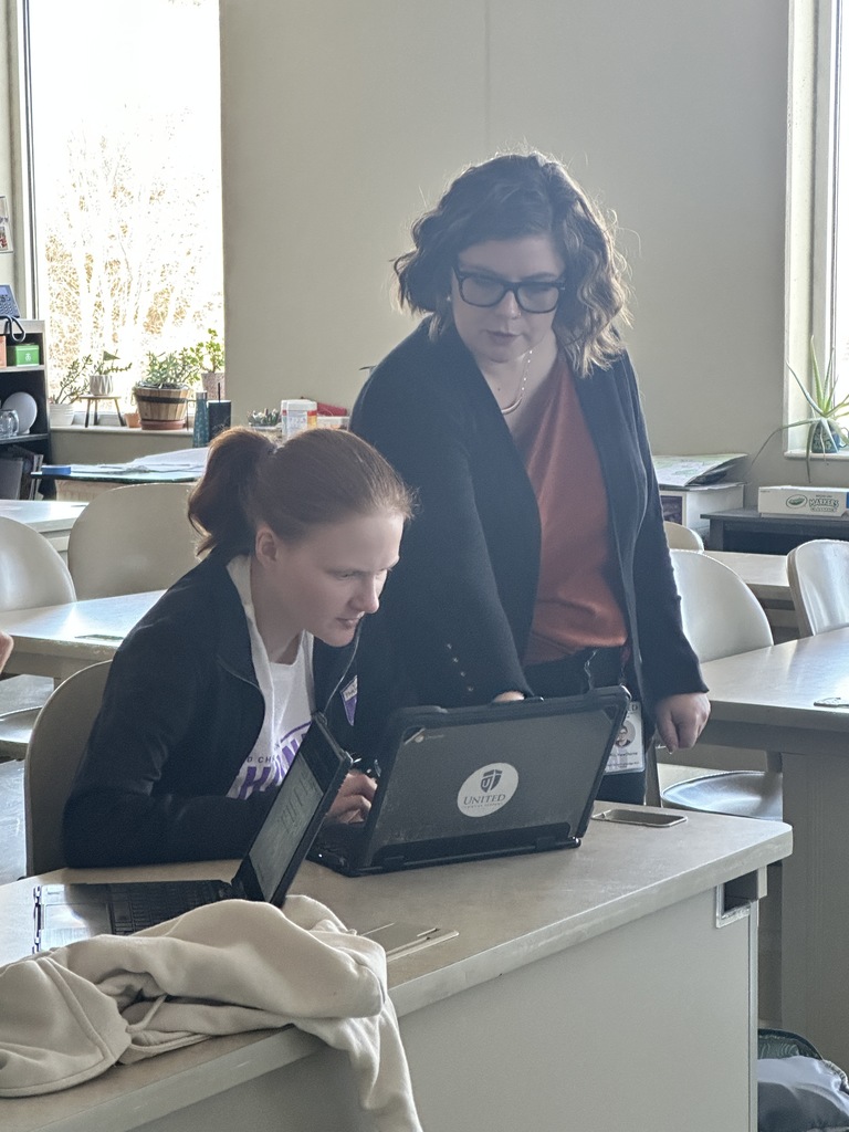 student at her desk being helped by a teacher